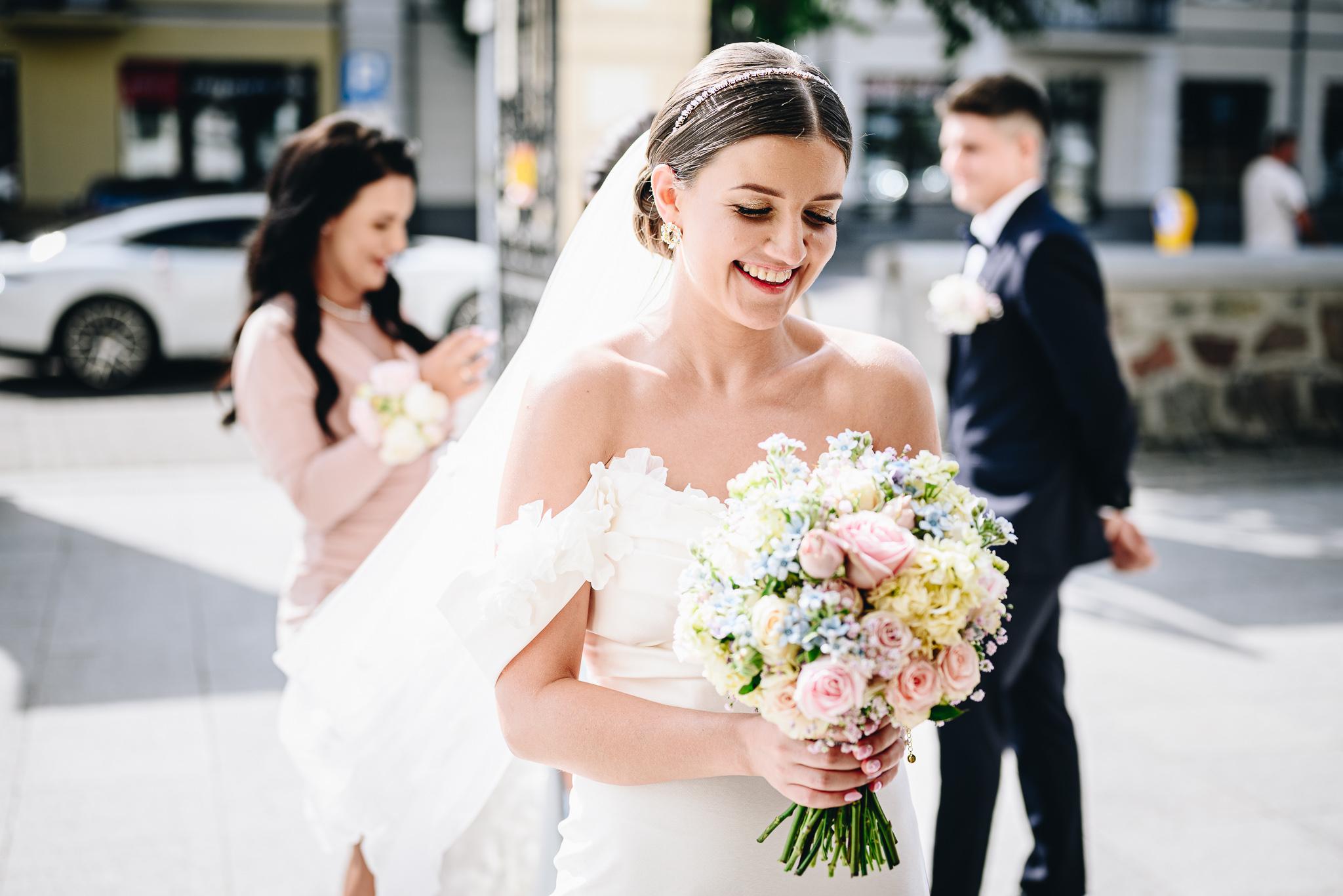 Uśmiechnięta panna młoda z bukietem czeka przed kościołem na ślub