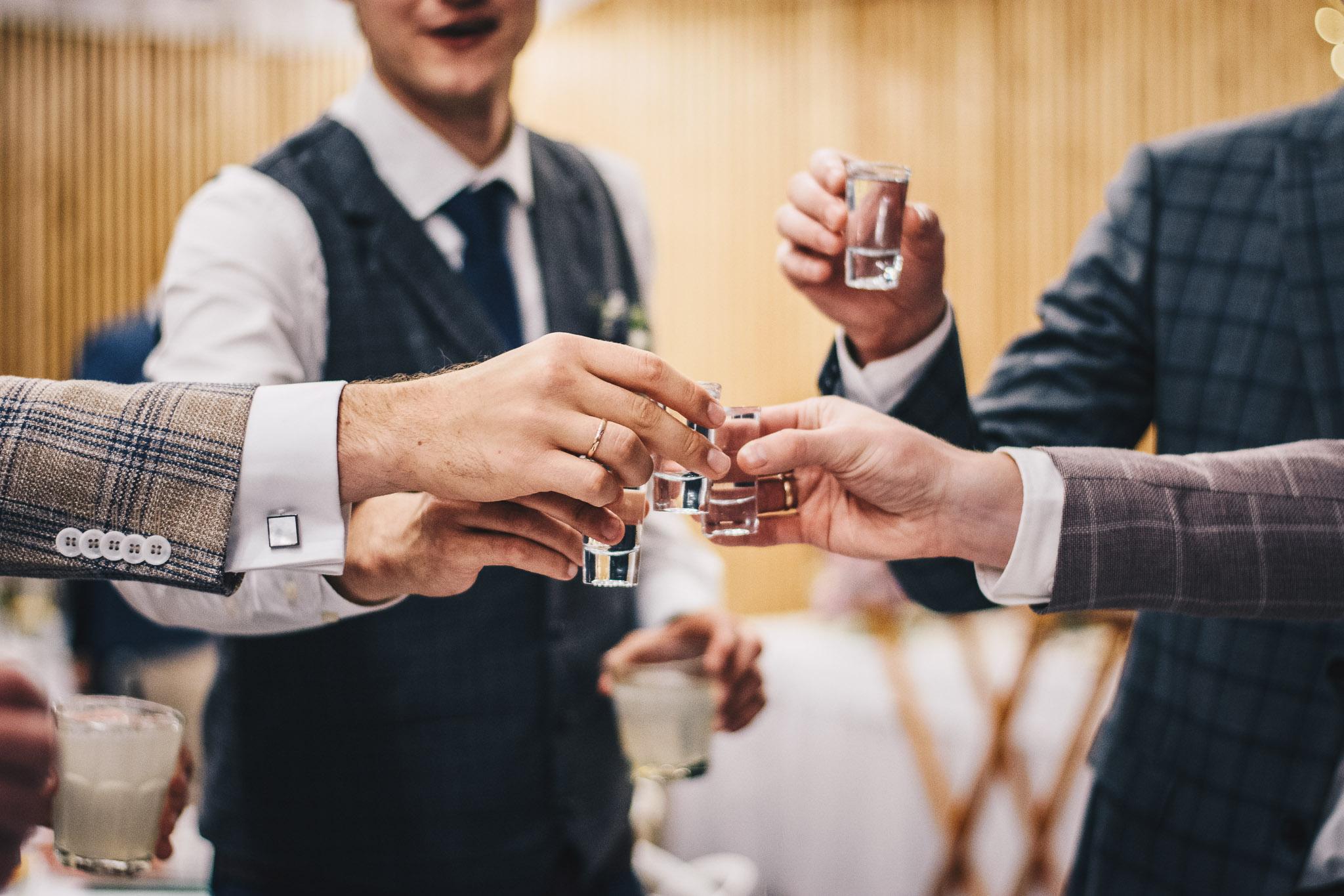 Mężczyźni wznoszą toast, stukając się kieliszkami wódki weselnej.