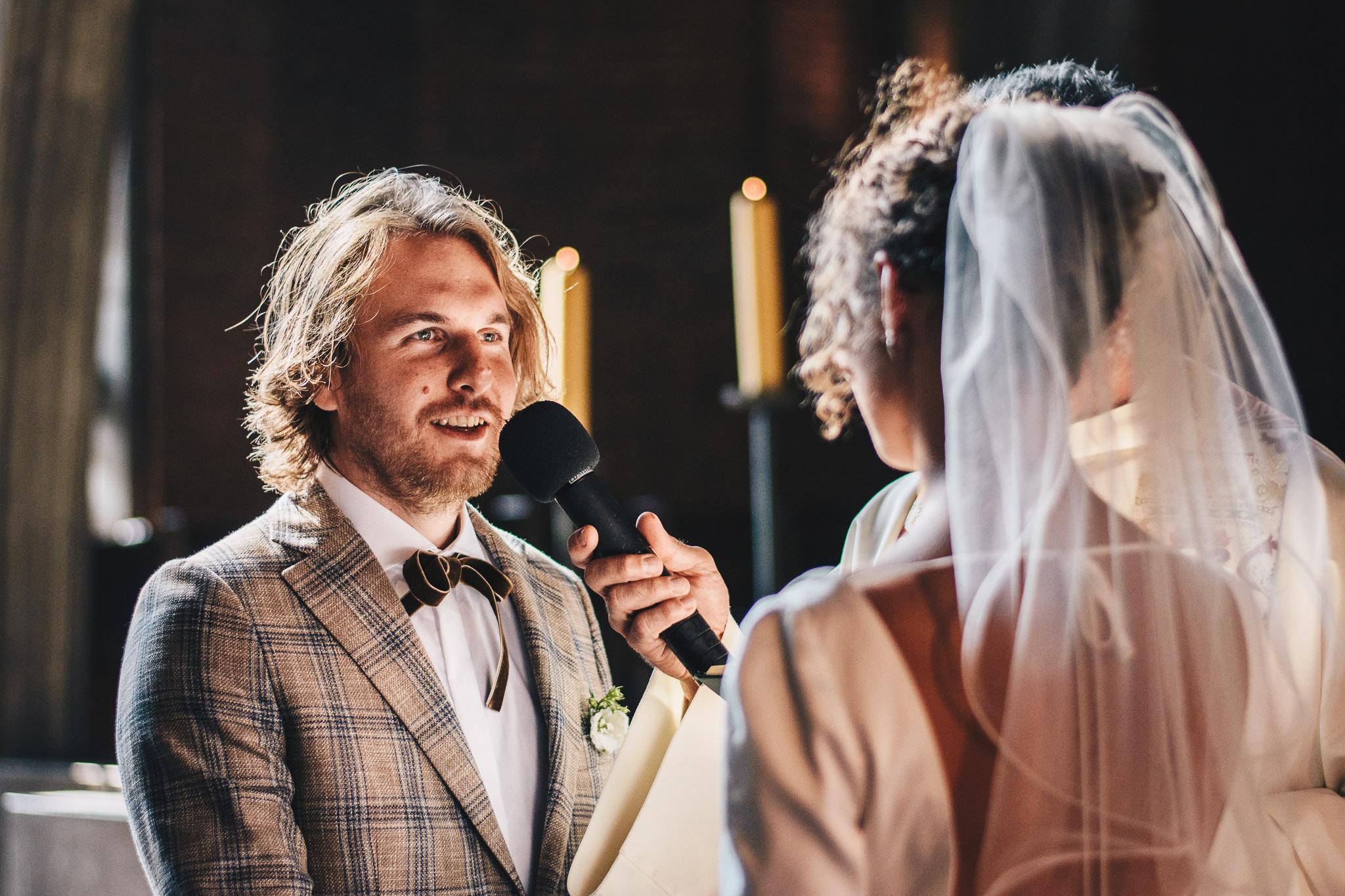 Przysięga ślubna. Pan młody patrzy na żonę i mówi do mikrofonu