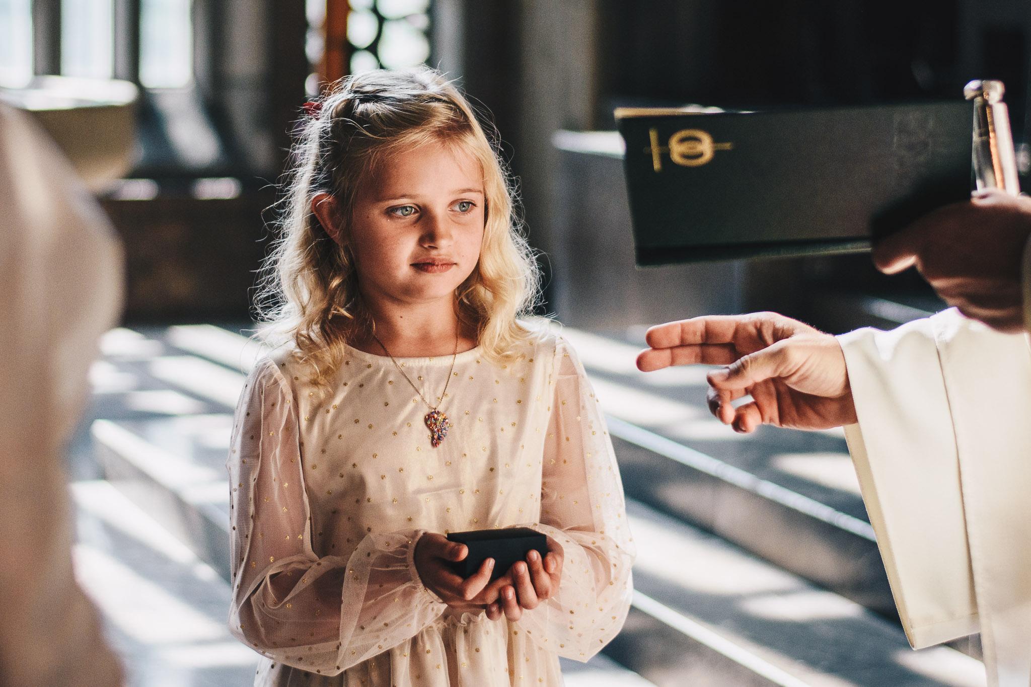 Dziewczynka w jasnej sukience trzyma pudełeczko z obrączkami podczas ślubu