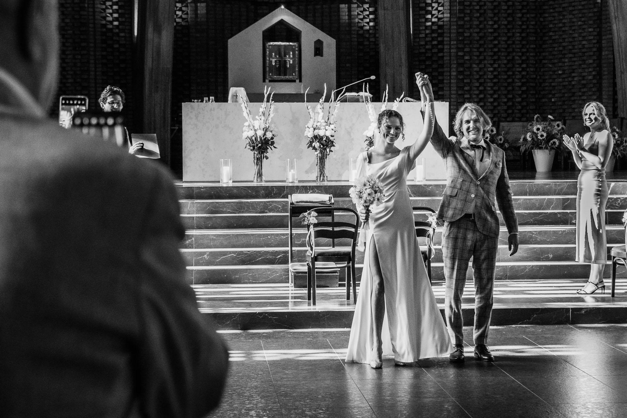 Nowożeńcy wznoszą ręce w geście radości, stojąc przed ołtarzem po ceremonii ślubnej.