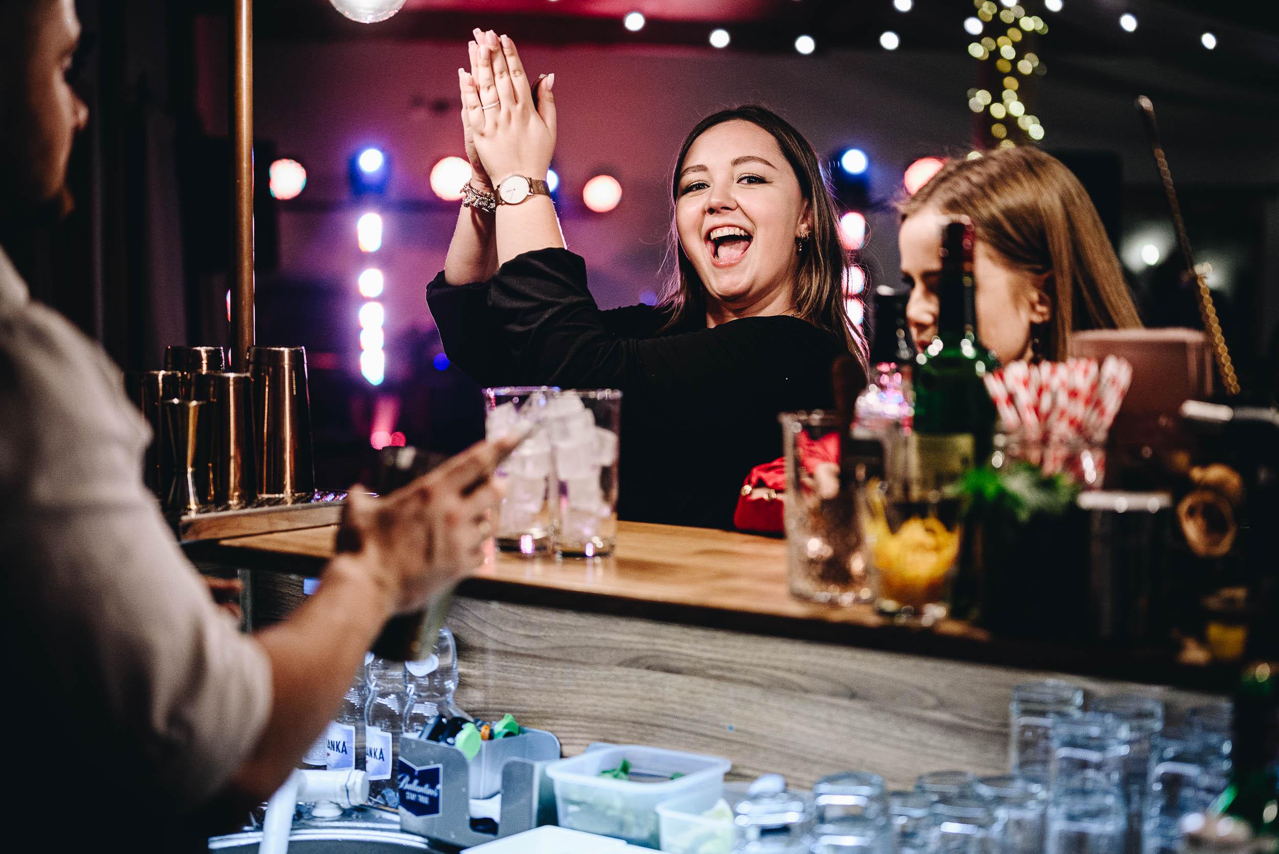 Kobieta klaszcze entuzjastycznie stojąc za barem na weselu.