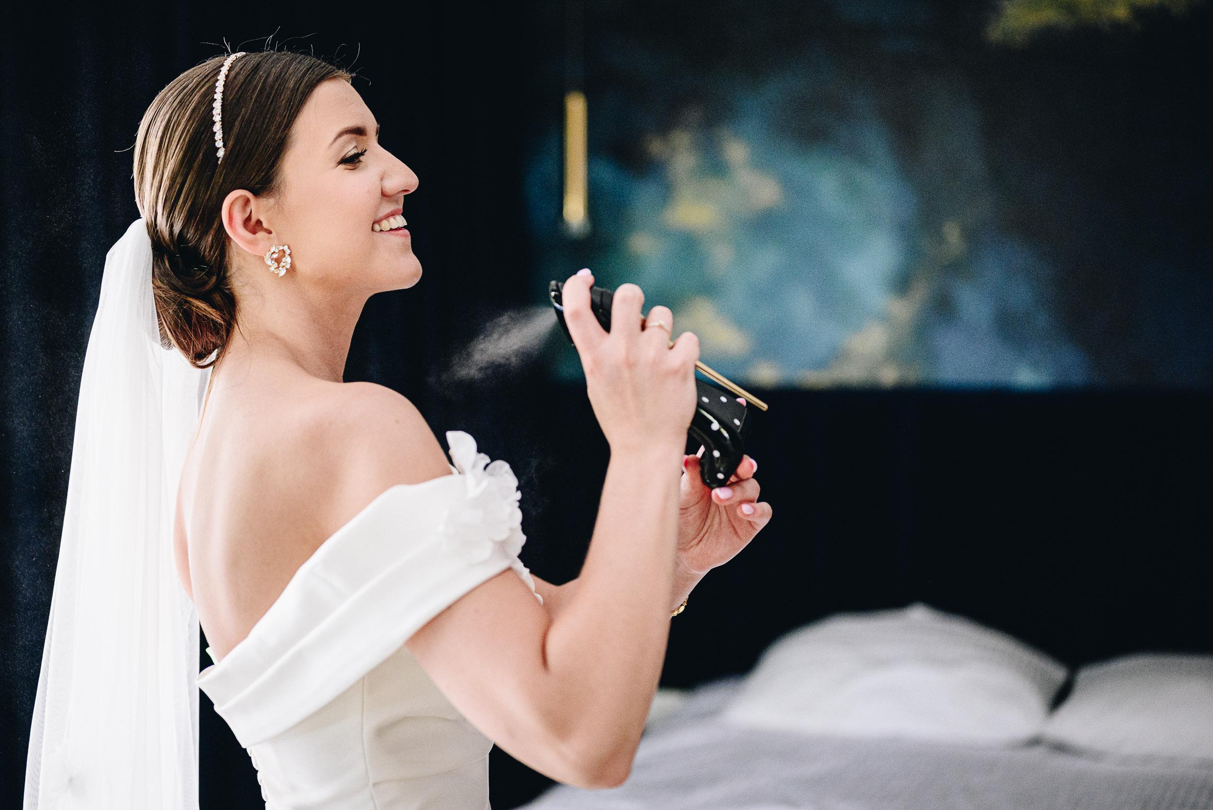 Panna młoda w sukni z odkrytymi ramionami perfumuje się podczas przygotowań