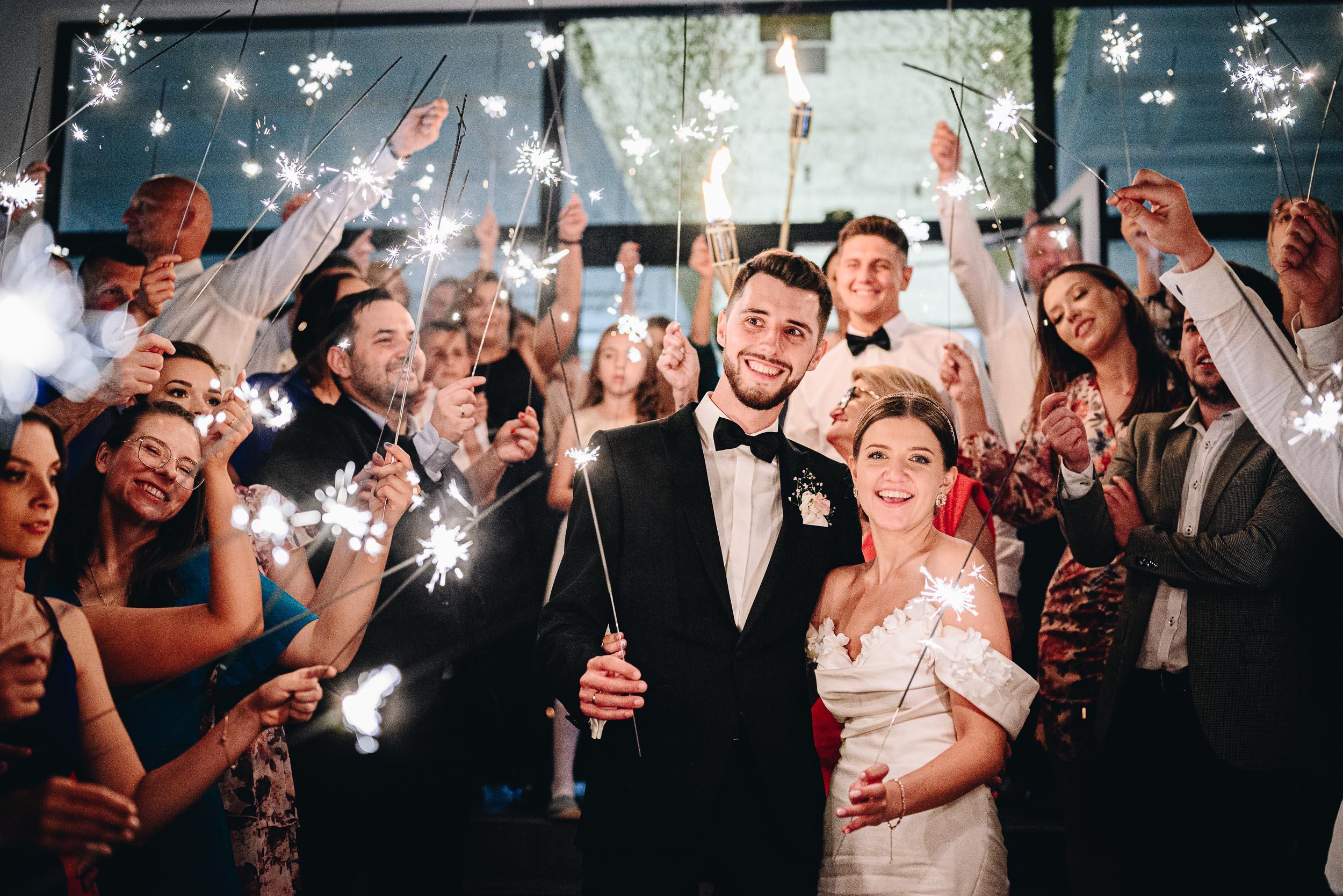 Grupowe zdjęcie z zimnymi ogniami. Na pierwszym planie uśmiechnięta młoda para