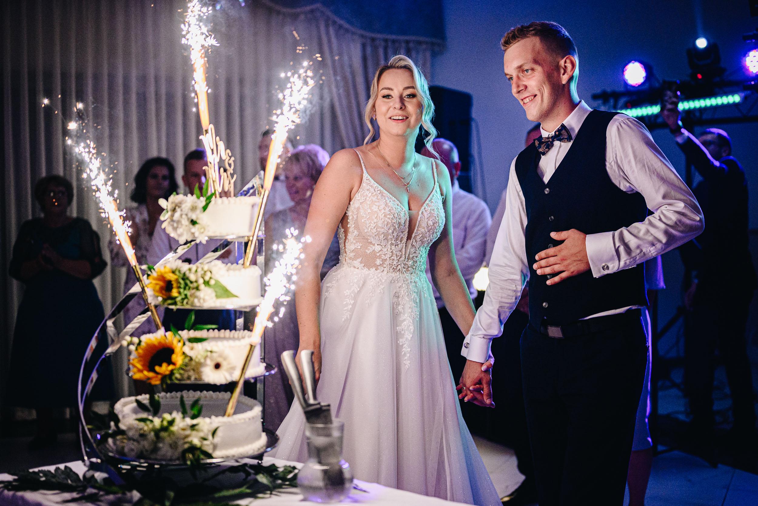 Szczęśliwa młoda para trzyma się za ręce przy świecącym torcie.