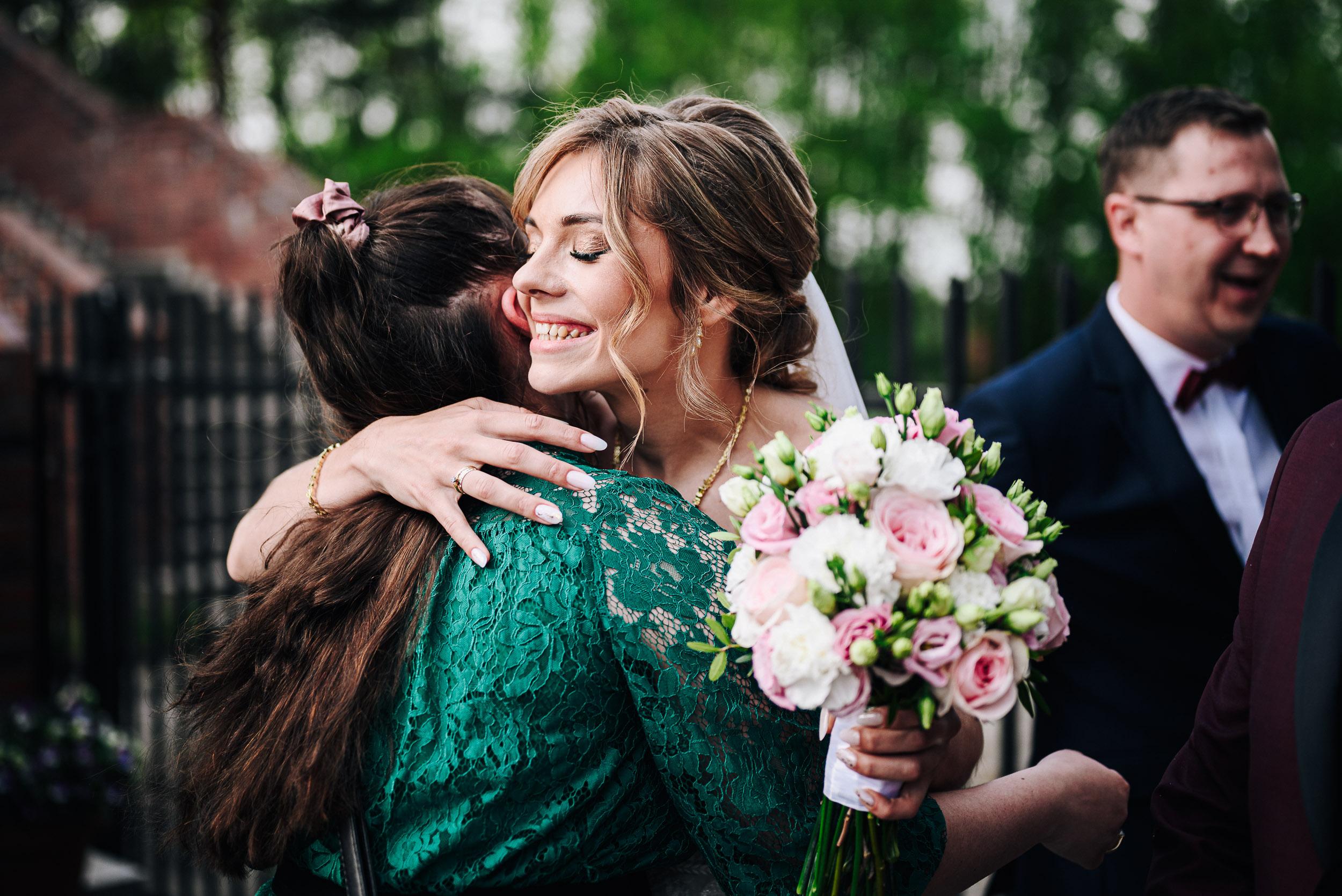 Uśmiechnięta panna młoda z bukietem ślubnym przytula gościa weselnego