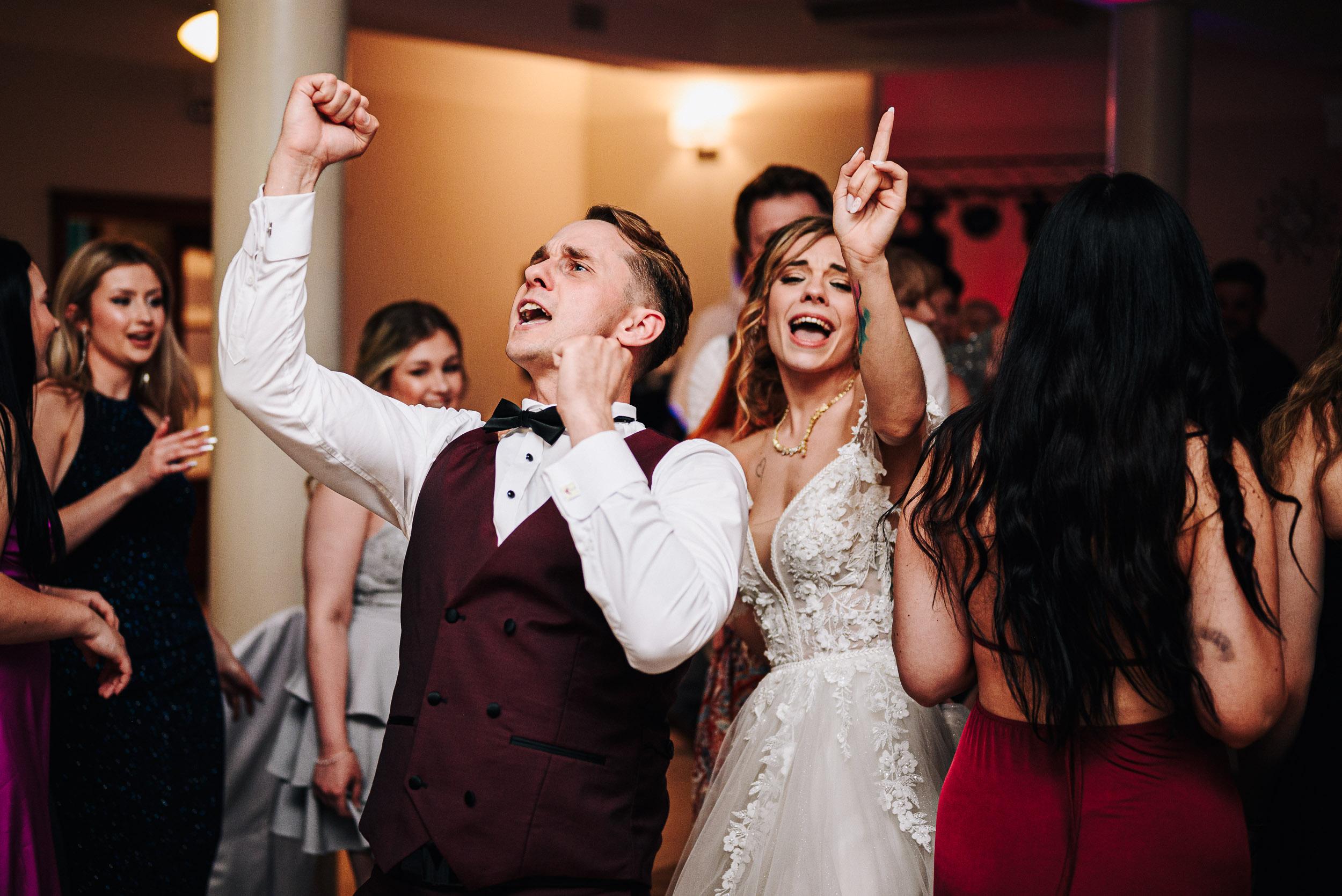 Goście i para młoda entuzjastycznie tańczą i bawią się na parkiecie.