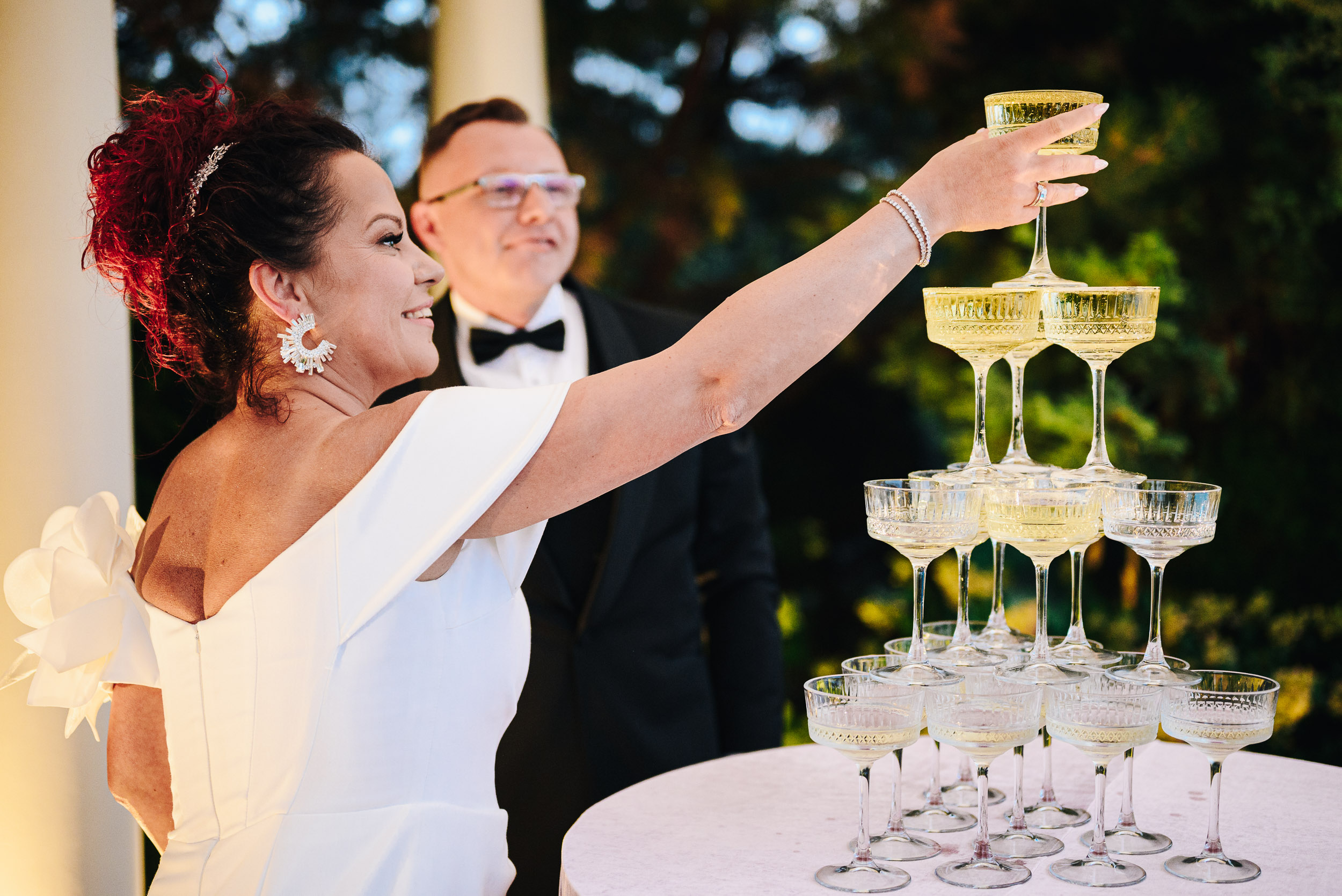 Panna młoda podnosi kieliszek z szampanem ze szczytu piramidy z kieliszków