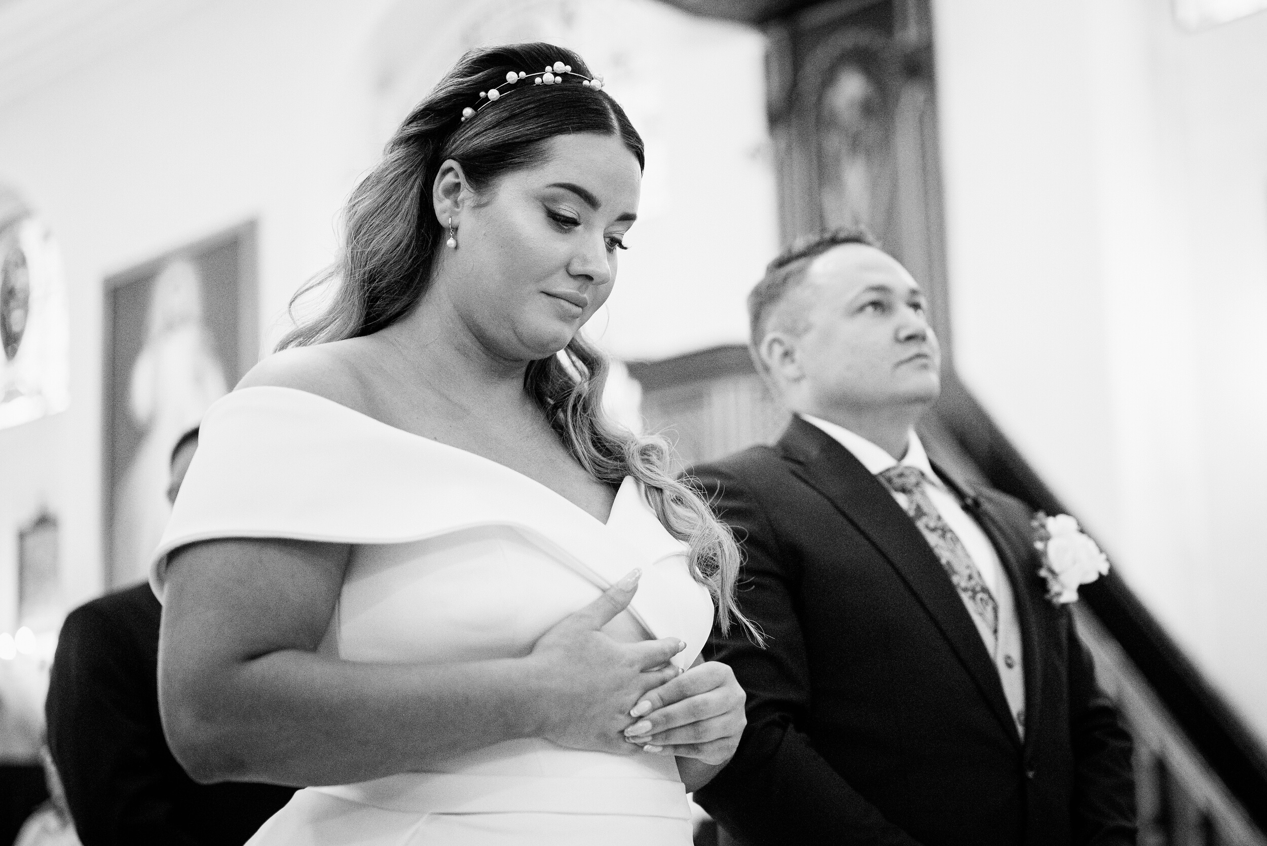 Panna młoda patrzy w ziemię i poprawia obrączkę ślubną. W tle pan młody patrzący w górę.